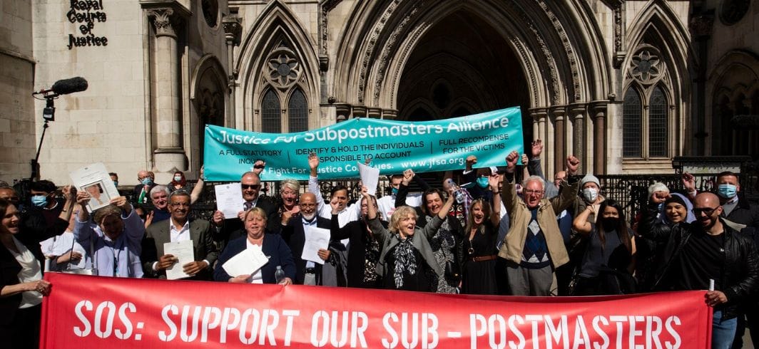 Post office Horizon sub postmasters celebrating outside Court of Justice holding red banner "SOS: Suppoty our sub postmasters".