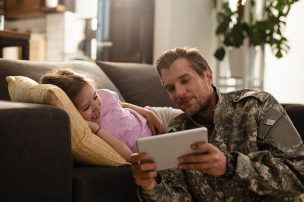 happy army soldier and his daughter using touchpad in the living room representing military injury compensation claims