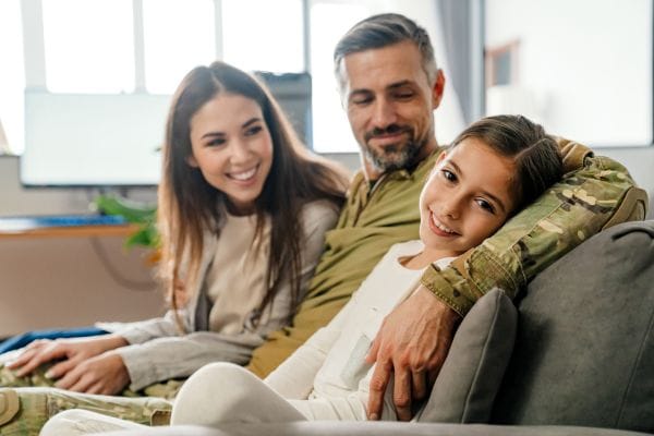 happy masculine military man hugging his family while sitting on sofa representing military injury claims compensation claims