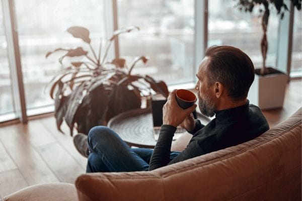 adult caucasian man sitting in a lounge chair in thought whilst drinking a coffee-concept-representing-domestic-violence-compensation-claims