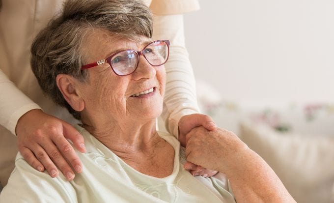 elderly lady on wheelchair holding hands with supporting volunteer standing behind her concept care home abuse claims
