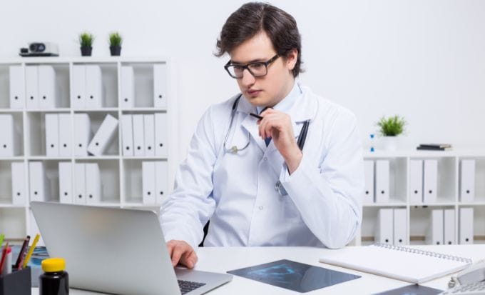doctor sat at a desk on his laptop and x rays on his desk concept medical negligence pregnancy and birth injury stillbirth and neonatal medication errors hospital negligence feature