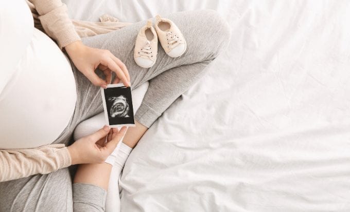 pregnant woman sat crossed legged looking at her ultrasound picture with baby booties on her knee concept medical negligence pregnancy and birth injury stillbirth and neonatal feature