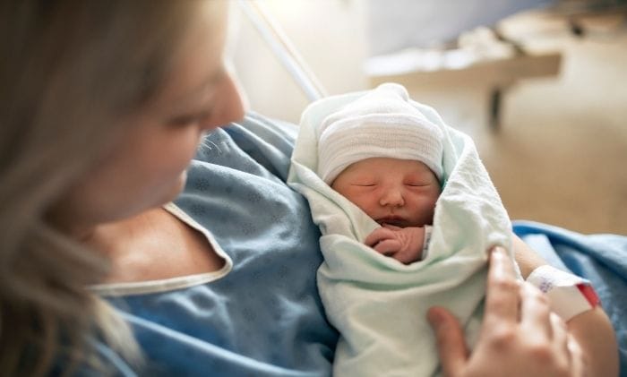 mother in hospital gown holding her newborn baby–concept representing medical negligence birth injury compensation claims