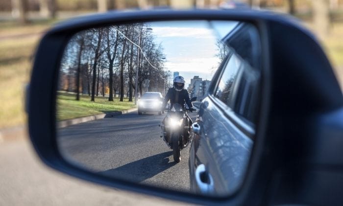 view looking behind from car side mirror with a motorcycle rider in view representing motorbike accident compensation claims